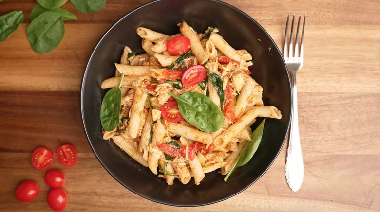 Pasta s rajčaty, špenátem v černé misce na dřevěném stole.