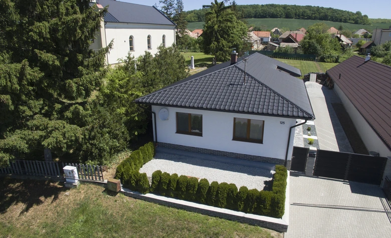 Modern dům s tmavou taškovou střechou v zalesněné oblasti.
