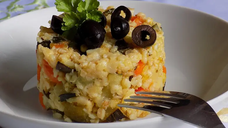 Připravený bulgur s zeleninou a černými olivami na talíři