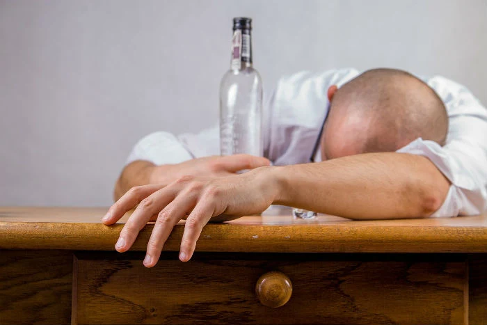 Muž ležící na stole s prázdnou lahví alkoholu