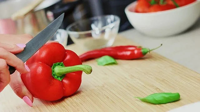 Ruka řeže červenou papriku na dřevěné desce