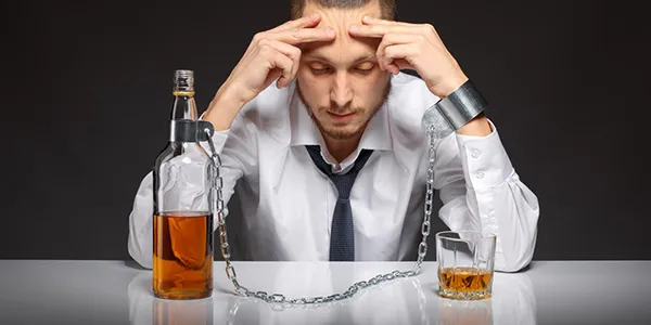 Muž řetězem spjatý s láhví alkoholu, znázorňující závislost