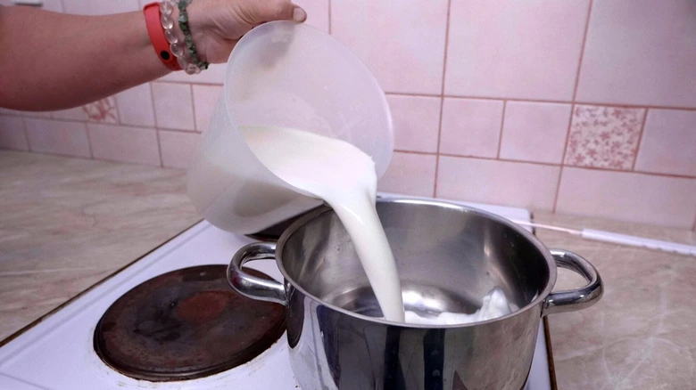 Nalévání mléka do hrnce při výrobě domácího sýra.