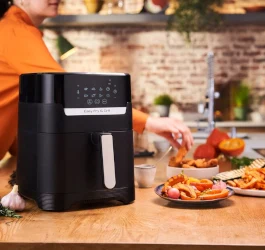 Černá horkovzdušná fritéza s čerstvými bramborami na kuchyňském stole.