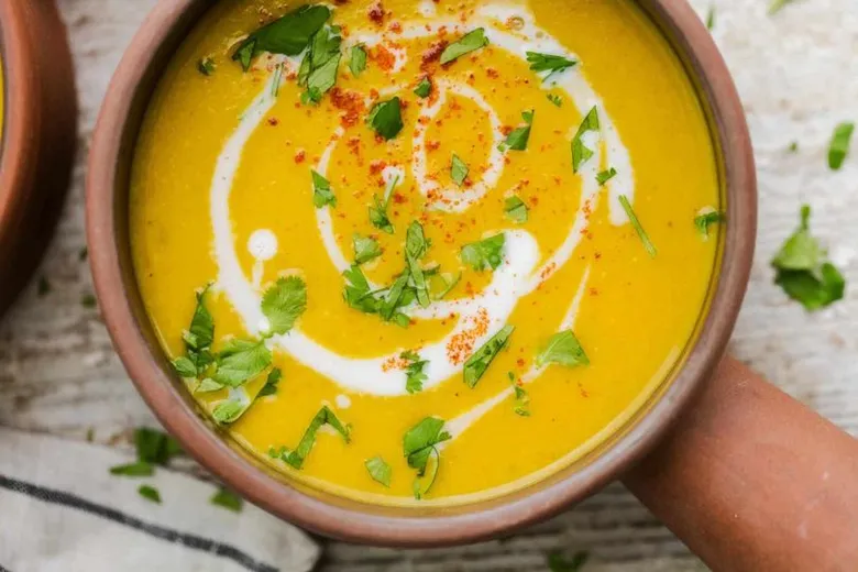 Hot yellow squash soup served in earthenware bowl