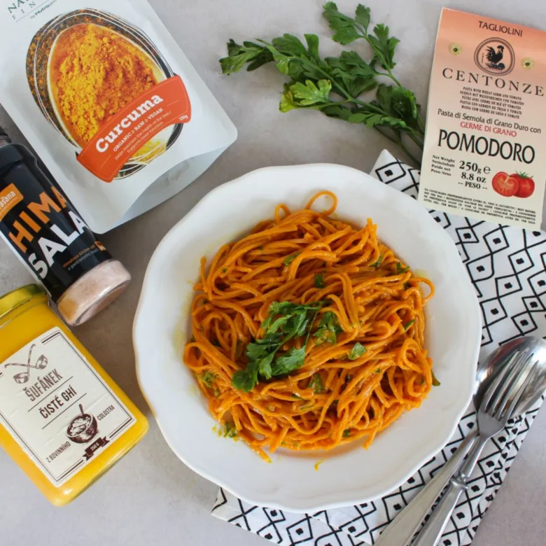 Pasta s turmeric omáčkou v bílé misce se zeleninou.