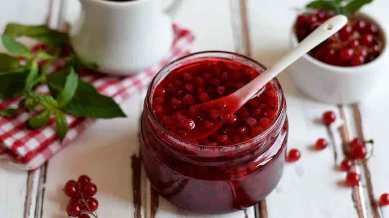 Skleněná dóza s červeným džemem z jahod, okolo čerstvé bobule a mátové listy