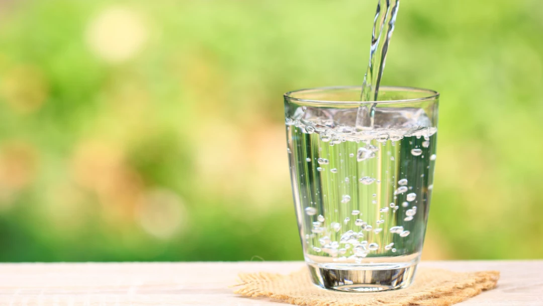 Voda se nalévá do sklenice na dřevěném stole venku