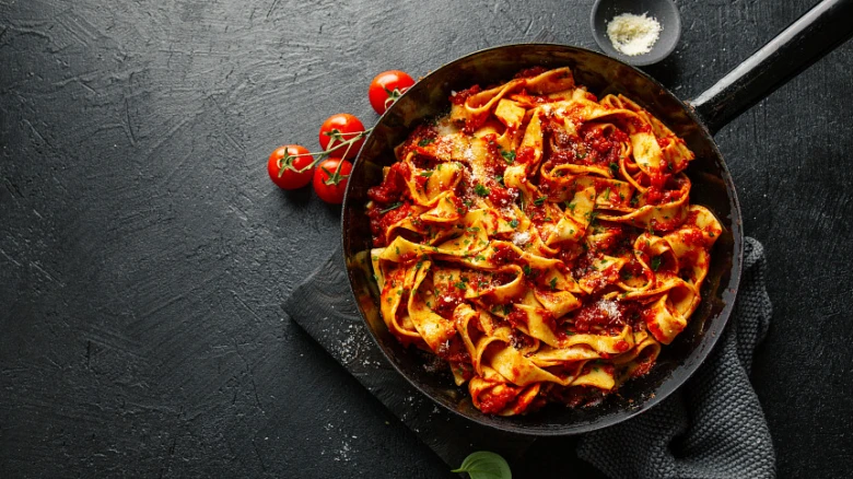 Pasta s rajčatovou omáčkou v pánvi na tmavém podkladu.