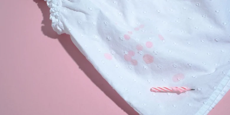Bílý ubrus s rozlitým voskem od svíčky na růžovém pozadí.
