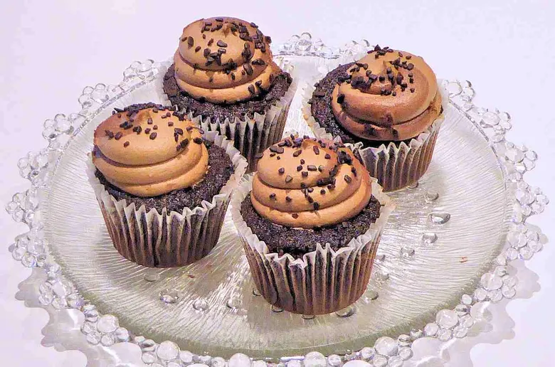 Čtyři čokoládové muffiny s krémem na skleněném podstavci.
