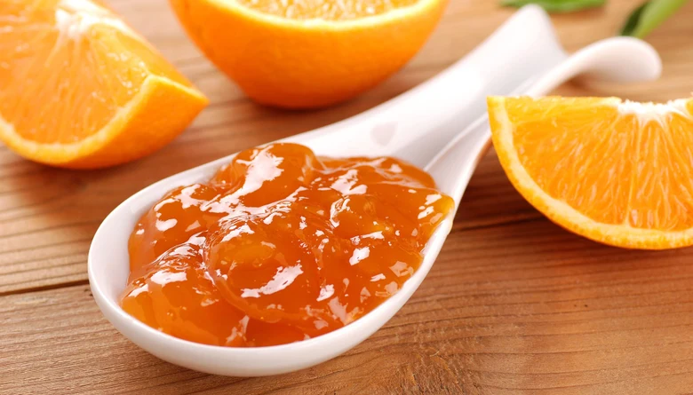 Domácí pomerančová marmeláda v lžíci s čerstvými plátky.