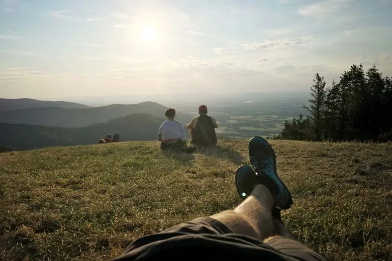 Turisté sedí na kopci s výhledem do údolí při západu slunce.