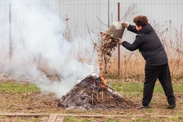 Muž pálí listí na zahradě, vzniká kouř