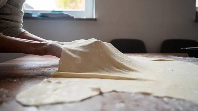 Ruce rolovají těsto na štrúdl na dřevěném stole