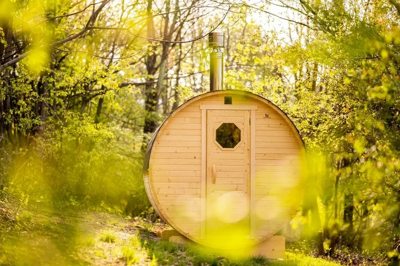 Venkovní dřevěná sauna v přírodě mezi stromy.