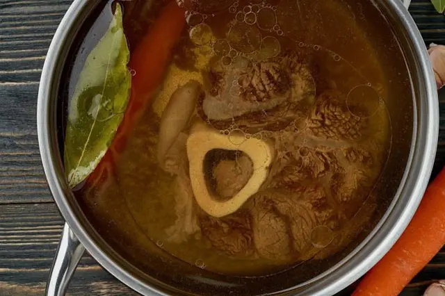 Hovězí vývar s kostmi, mrkví a listem v hrnci