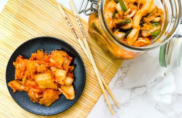 Korejské zelí v sklenici vedle talíře s čínskou kuchyní.