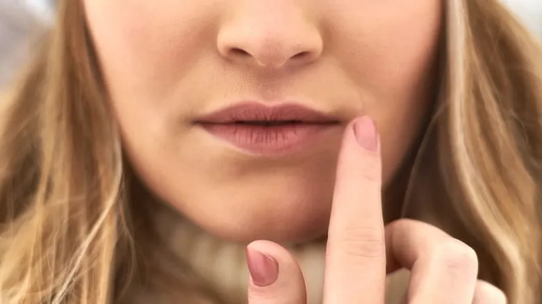 Žena ukazuje prstem na popraskaný koutek rtu.