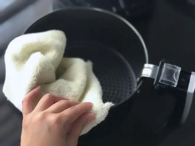 Ruční čištění košíku horkovzdušné fritézy utěrkou.