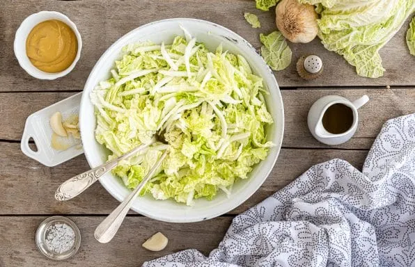 Hotový salát z pekingského zelí s přílohami na dřevěném stole.