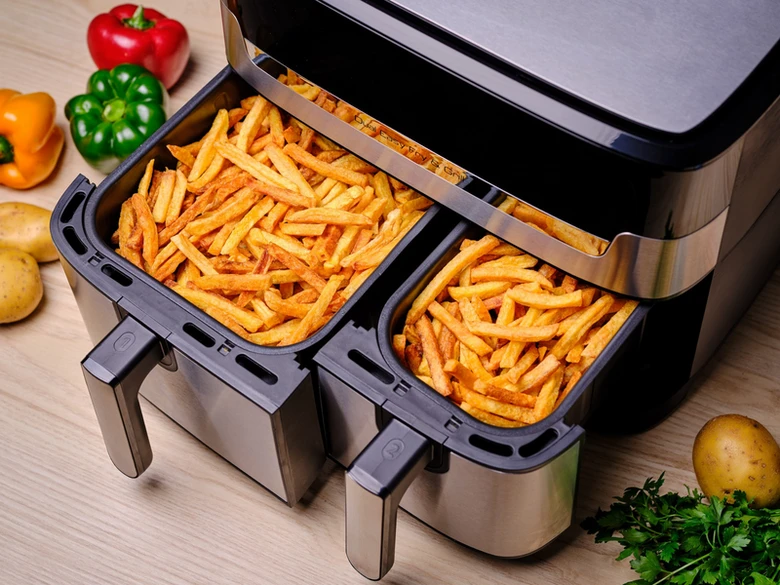 Horkovzdušná fritéza plná hranolů s čerstvými zeleninami.