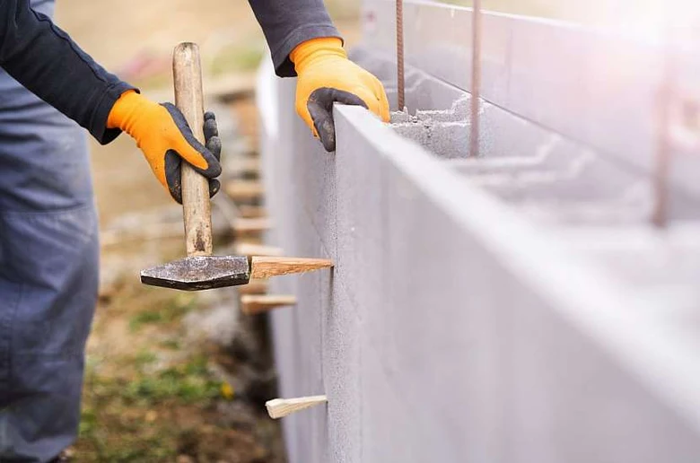Stavebník upravuje bednění z betonových bloků kladivem.