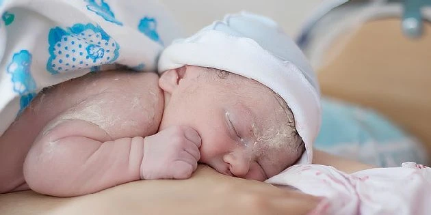 Spící novorozené miminko v bílé čepici na rukou.