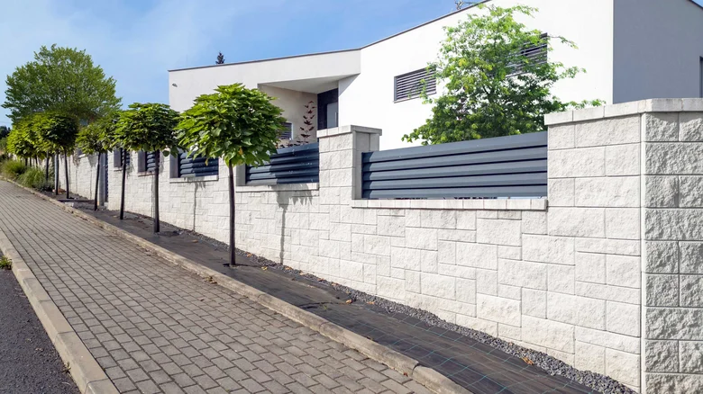Bílý dům s kamenným plotem a stromy na chodníku