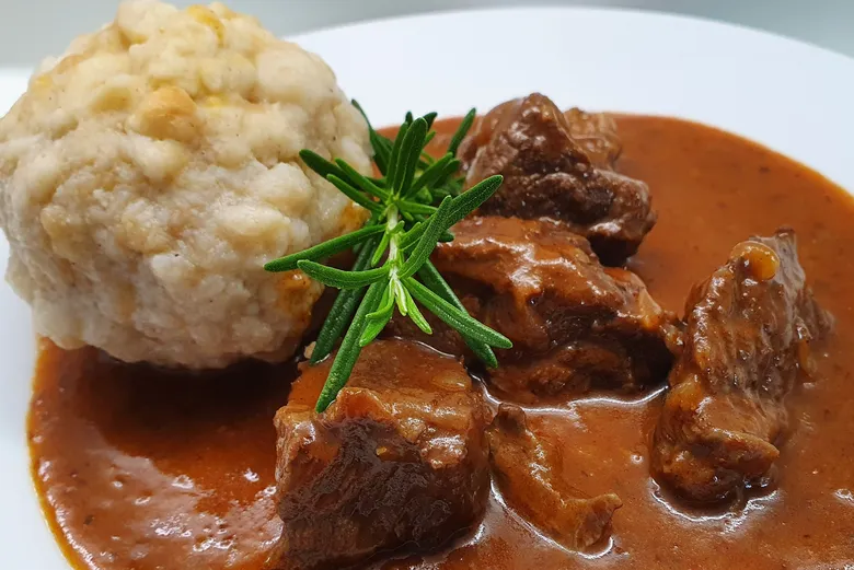Hotová pečená hovězí omáčka s knedlíky na bílém talíři.