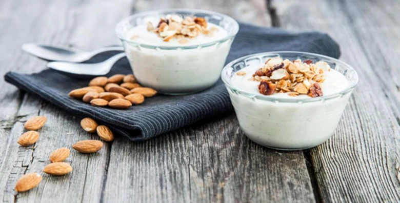 Dva skleněné misky jogurtu s ořechy na dřevěném stole.