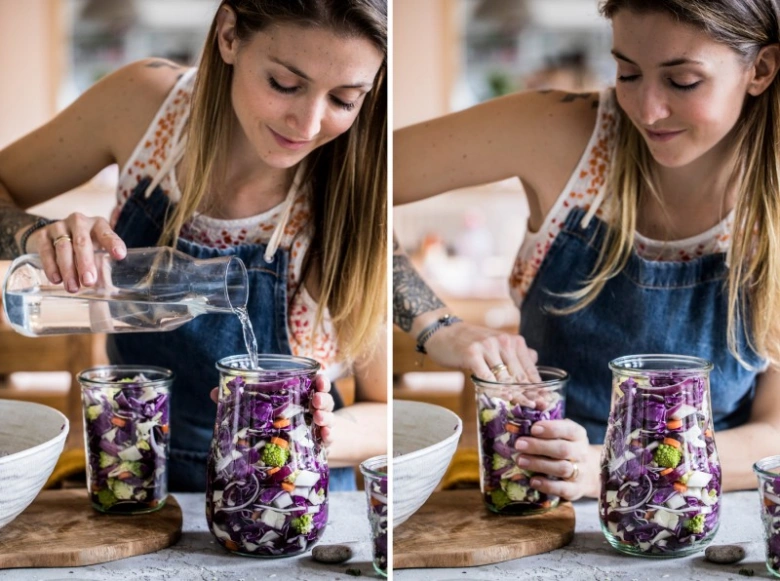 Žena nalévá vodu do sklenic s nakrájenou červenou kapustou pro fermentaci.