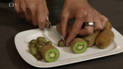 Ruce řezají čerstvého zeleného kiwi na bílém talíři.