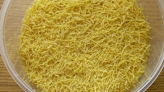 Sušené domácí nudle v průhledné mísce na dřevěném povrchu.