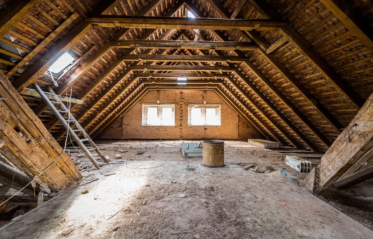 Neúplně zařízený podkroví s dřevěnými trámy a okny.