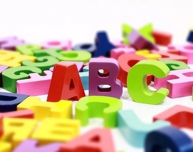 Barevné plastové písmena ABC rozsypaná na bílém povrchu.