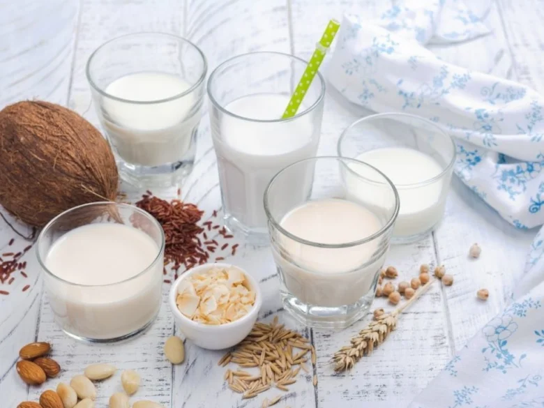Různé rostlinné mléka s jejich surovými ingrediencemi na bílém dřevě.