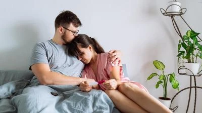 Muž a žena drží těhotenský test v posteli.