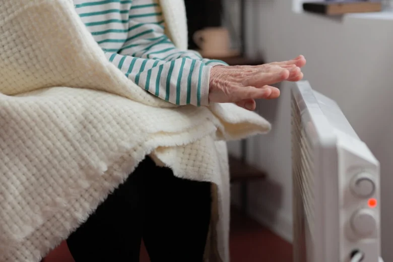 Starší osoba zahřívá ruce u elektrického topení.