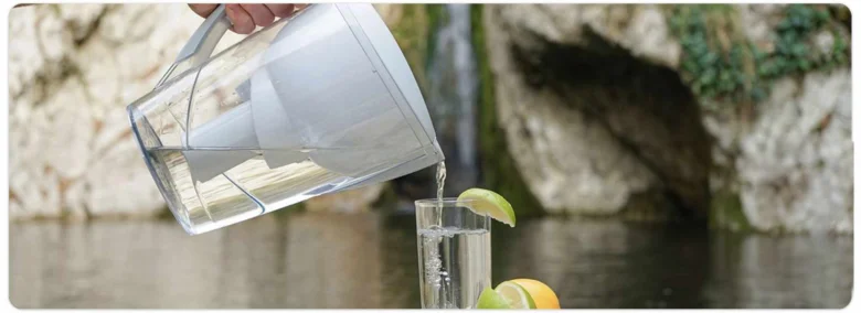 Ruka nalévá vodu z filtrační konvice do sklenice s citronem.