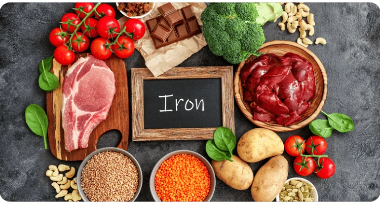 Různé železité potraviny jako játra, maso, čočka, špenát a brokolice kolem tabule s nápisem Iron