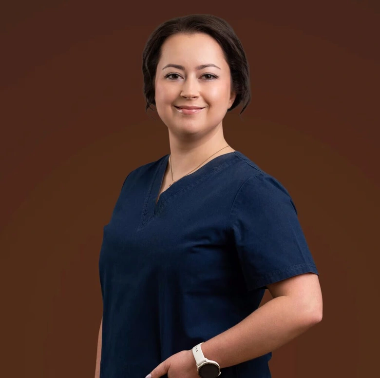 Žena v modrých lékařských uniformách se usmívá na fotografii.