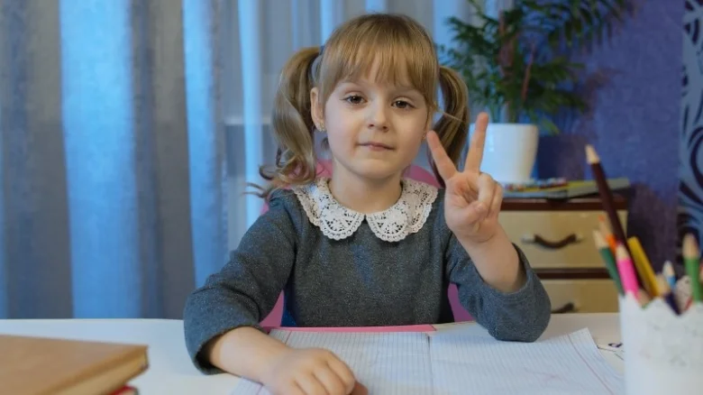 Dívka sedí u stolu s psacím materiálem pro děti.