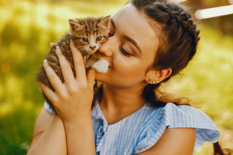 Dívka líbá malé koťátko, které drží v náručí.