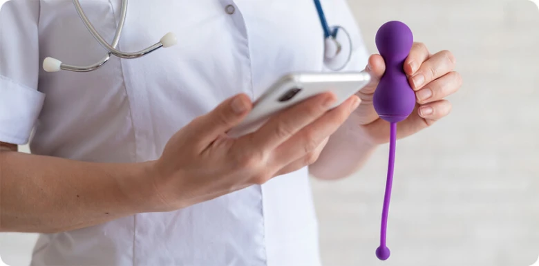 Lékař drží faložní dilatátor a telefon pro vzdělávací účely.