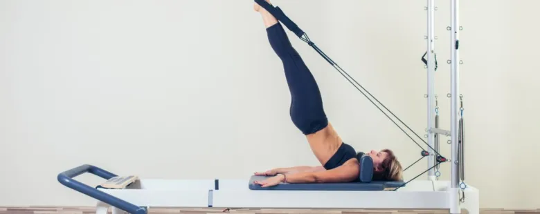 Žena cvičí pilates na přístroji reformér.
