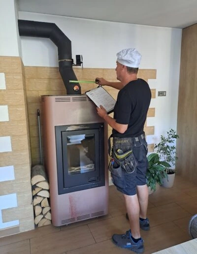 Muž provádí revizi komína s dokumentací u krbu.