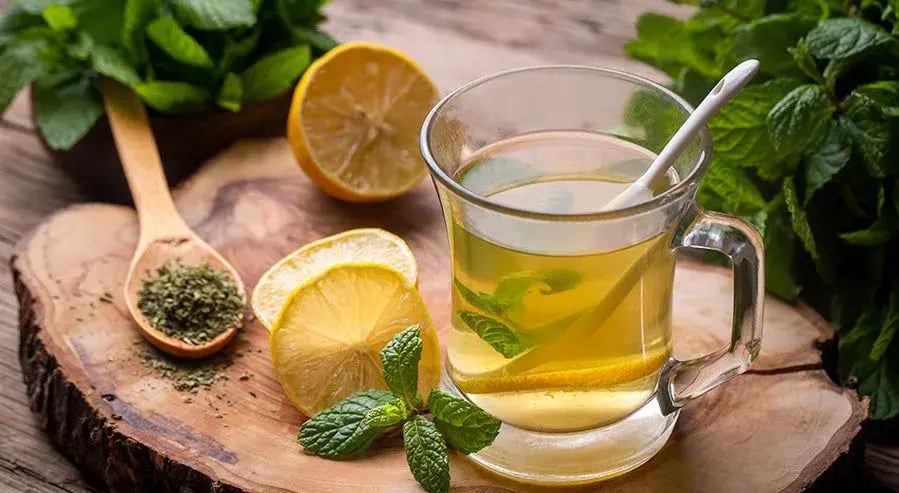 Sklenička s meduňkovým čajem, citrony a sušené listy na dřevěném podkladu.