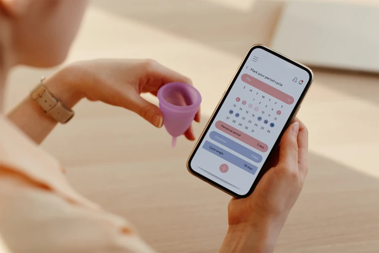 Žena drží menstruační šálku a aplikaci pro sledování cyklu.