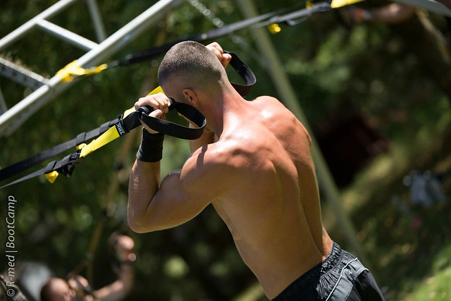 Muž cvičí na bicepsy pomocí TRX pásky venku.